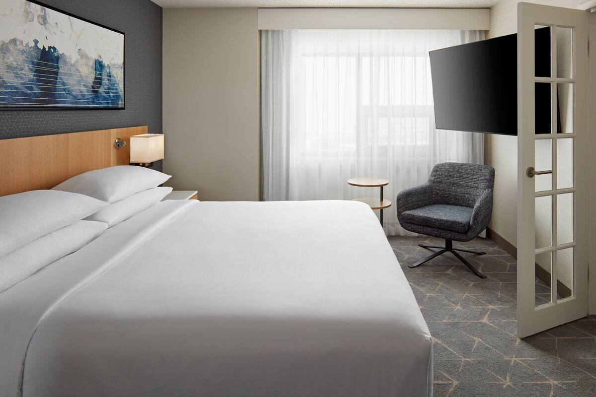 A hotel room with a large bed, a chair, a TV, and a door.