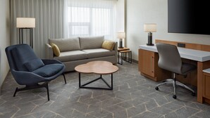 A hotel room with a sofa, two armchairs, a small wooden coffee table, a desk with a chair, a flat-screen TV, and two lamps. - Delta Hotels by Marriott Calgary Airport In-Terminal (Calgary)