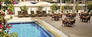 Un área junto a la piscina con sillones de descanso y sombrillas, suelo de baldosas y una piscina con borde de azulejos azules.