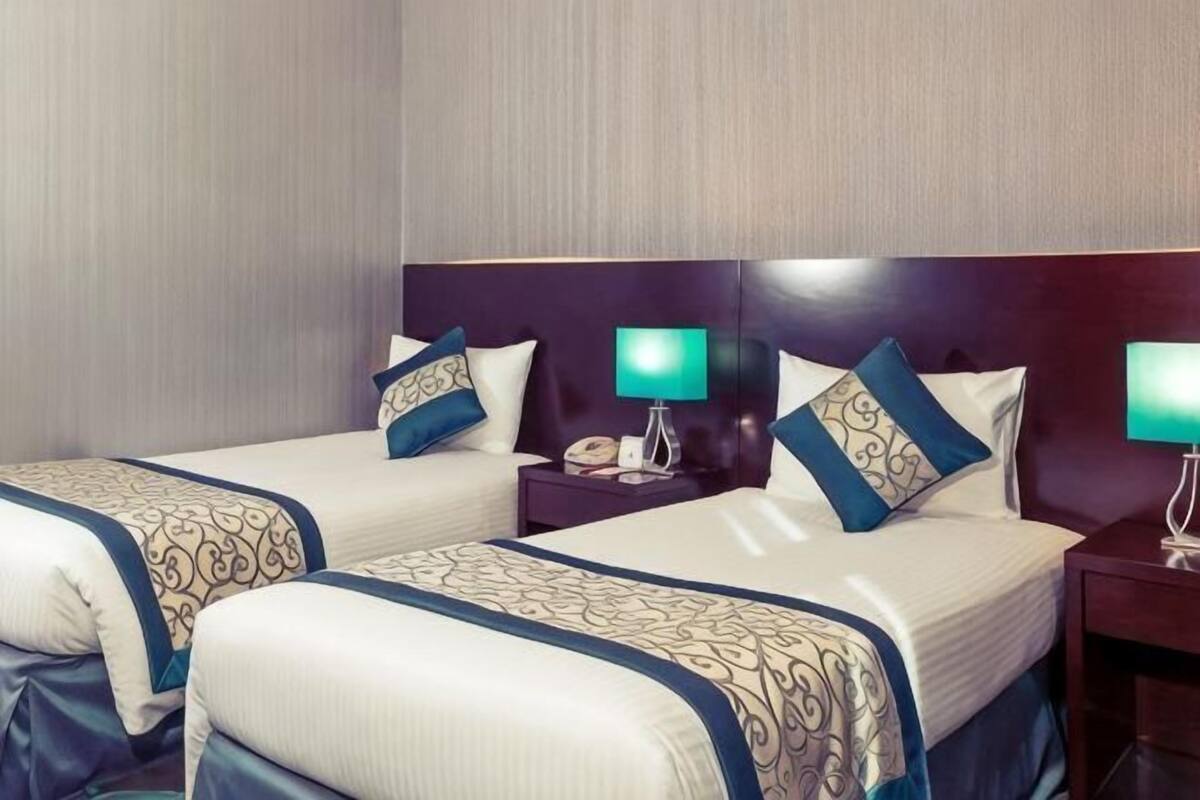 A hotel room with two beds, each with a headboard, bedside tables, and lamps.