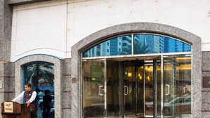Entrada de hotel con letrero con el nombre, zona de estacionamiento con chofer y puerta de cristal.