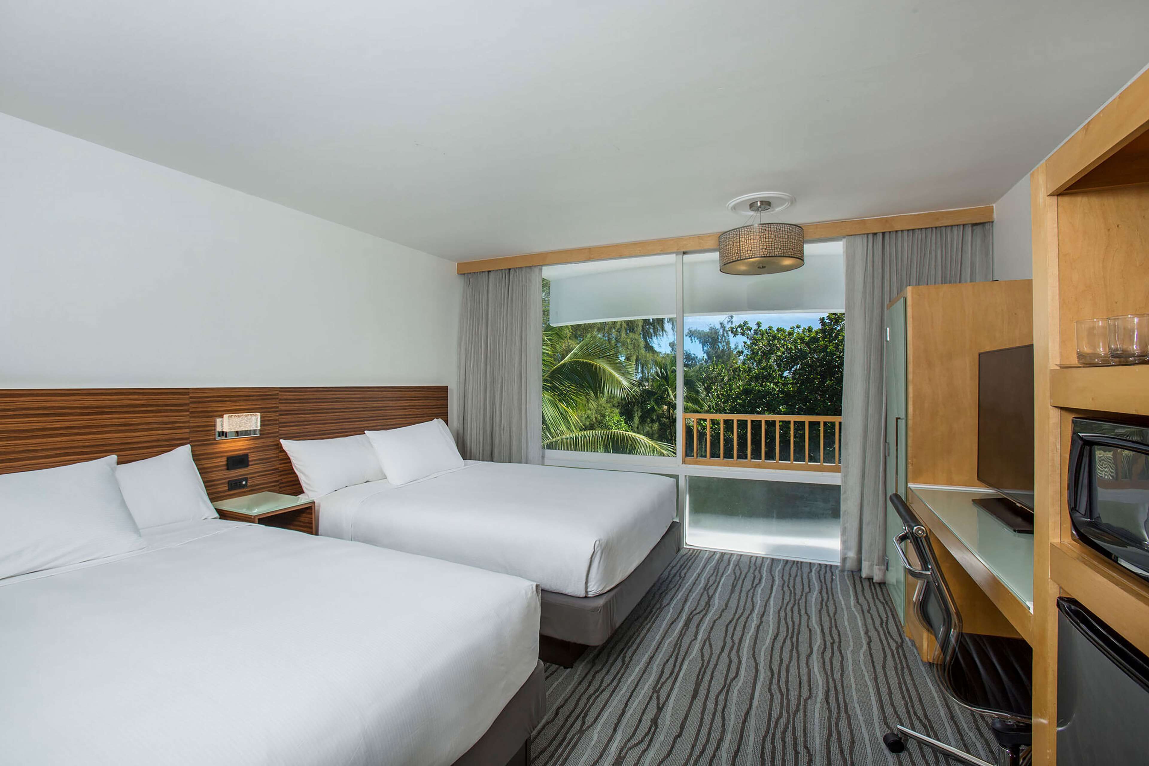 Hotelkamer met twee bedden, een televisie, een minibar en een balkon met uitzicht op groen.