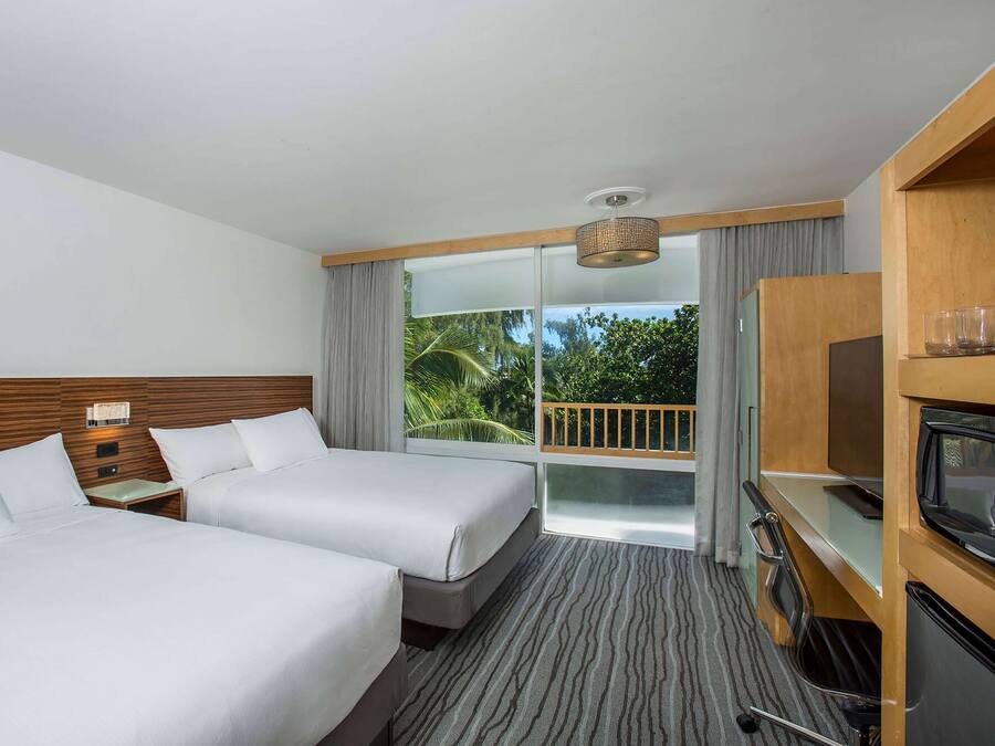Habitación de hotel con dos camas, televisor, minibar y balcón con vistas a zonas verdes.