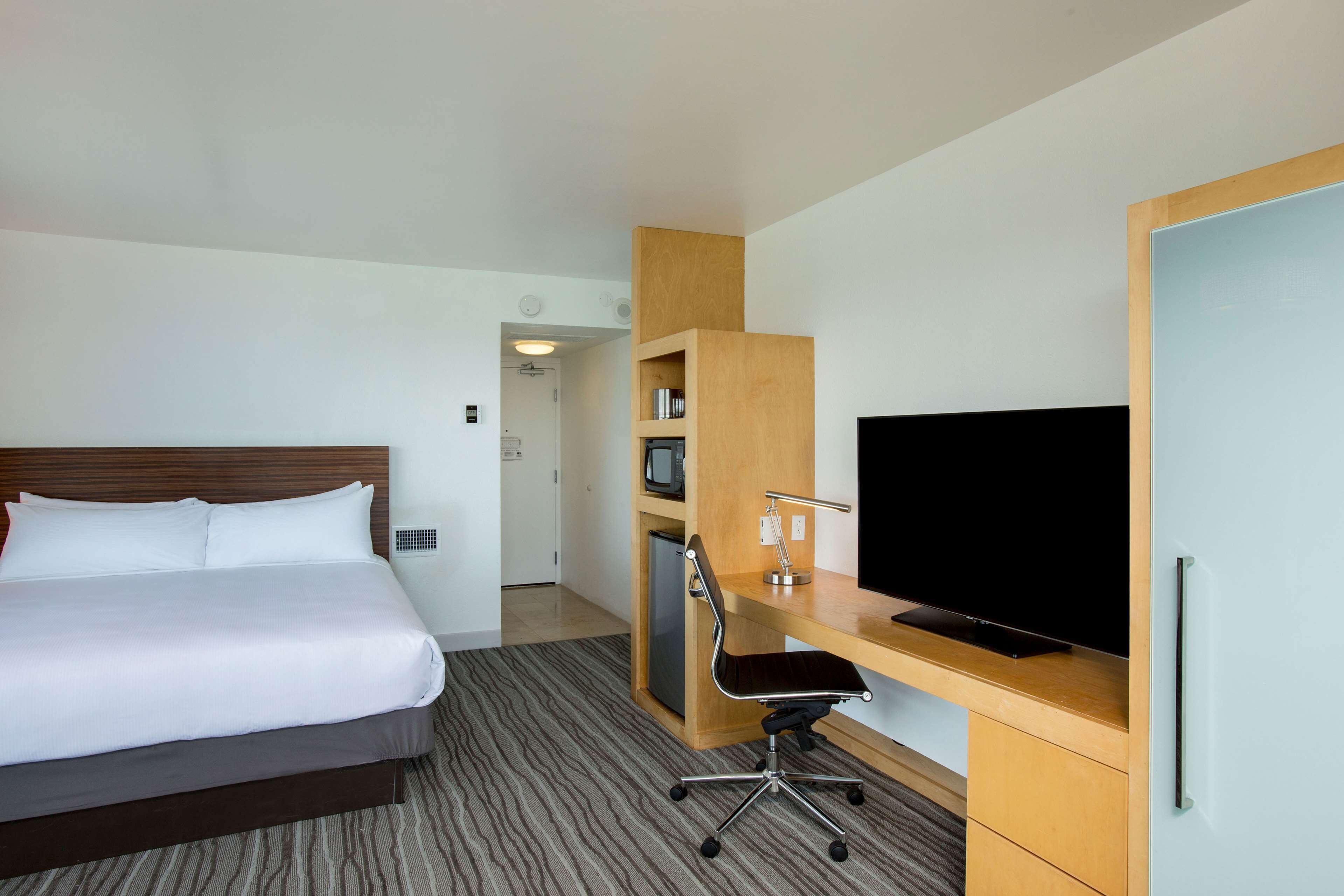 A hotel room with a bed, a desk, a television, and a small refrigerator.