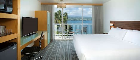 Ein Hotelzimmer mit Bett, Schreibtisch mit Fernseher, Minibar und einem Balkon mit Meerblick.