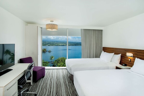 Habitación de hotel con dos camas, un escritorio con televisor y un ventanal que ofrece vistas a un cuerpo de agua y zonas verdes.