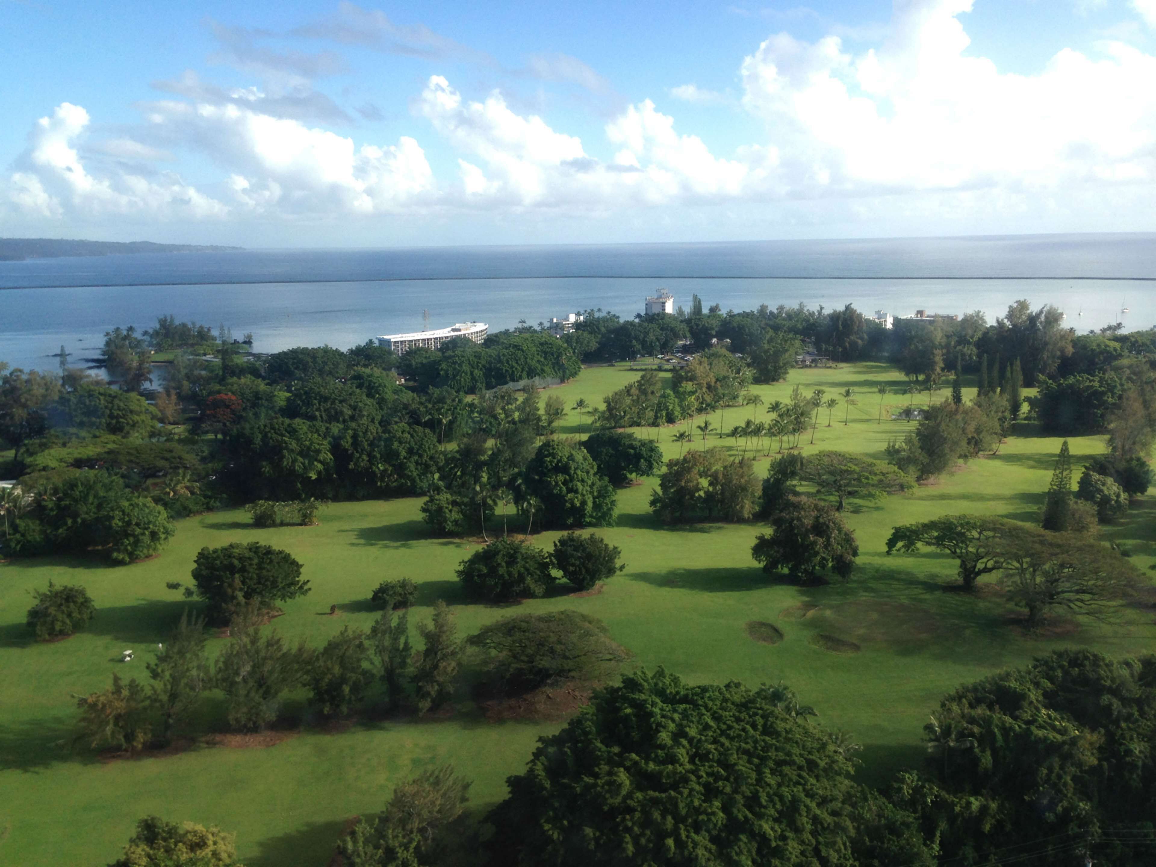 A golf course with a view of the ocean and a distant city skyline.
