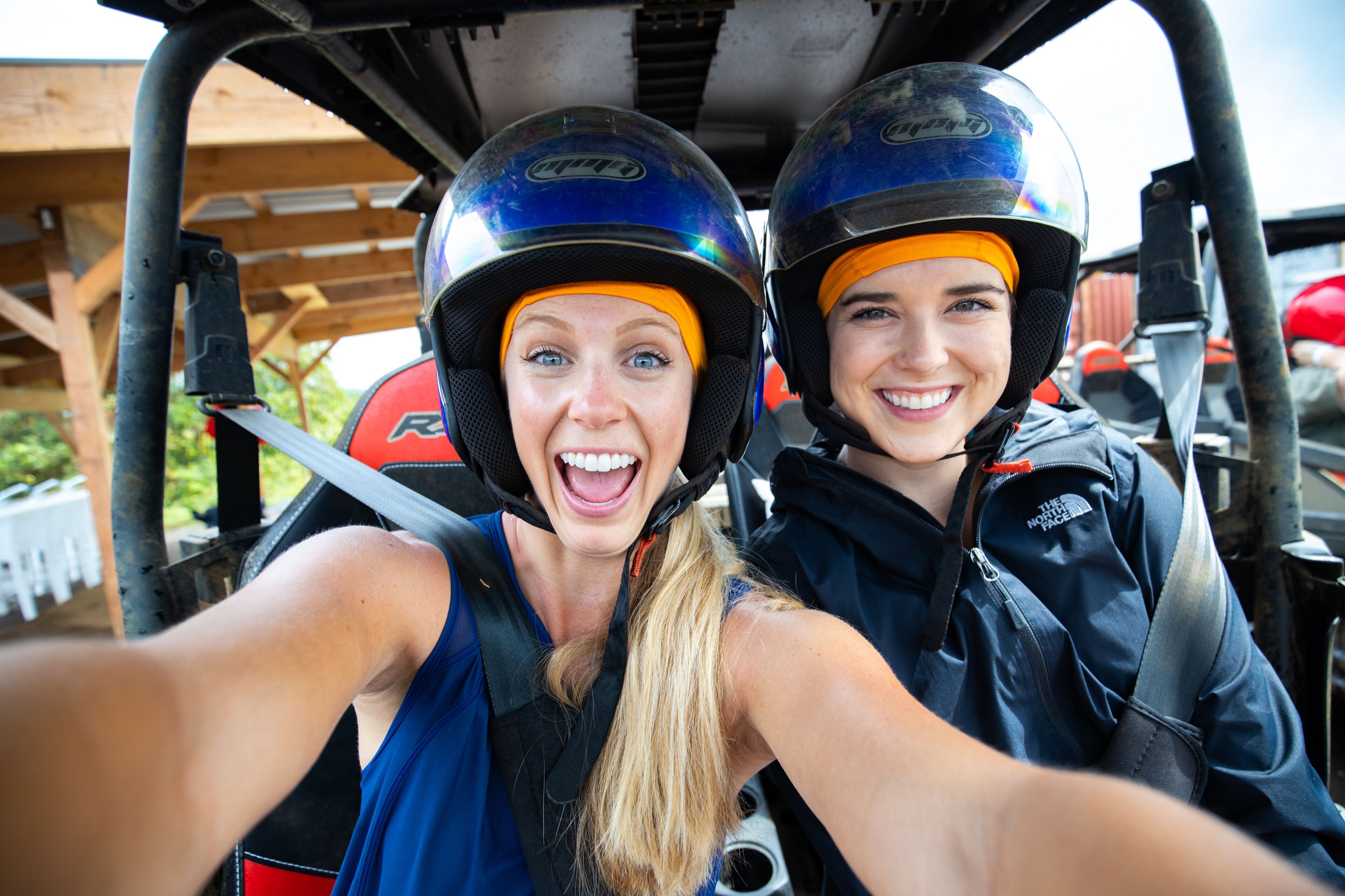 Two people in a vehicle with a wooden structure in the background.