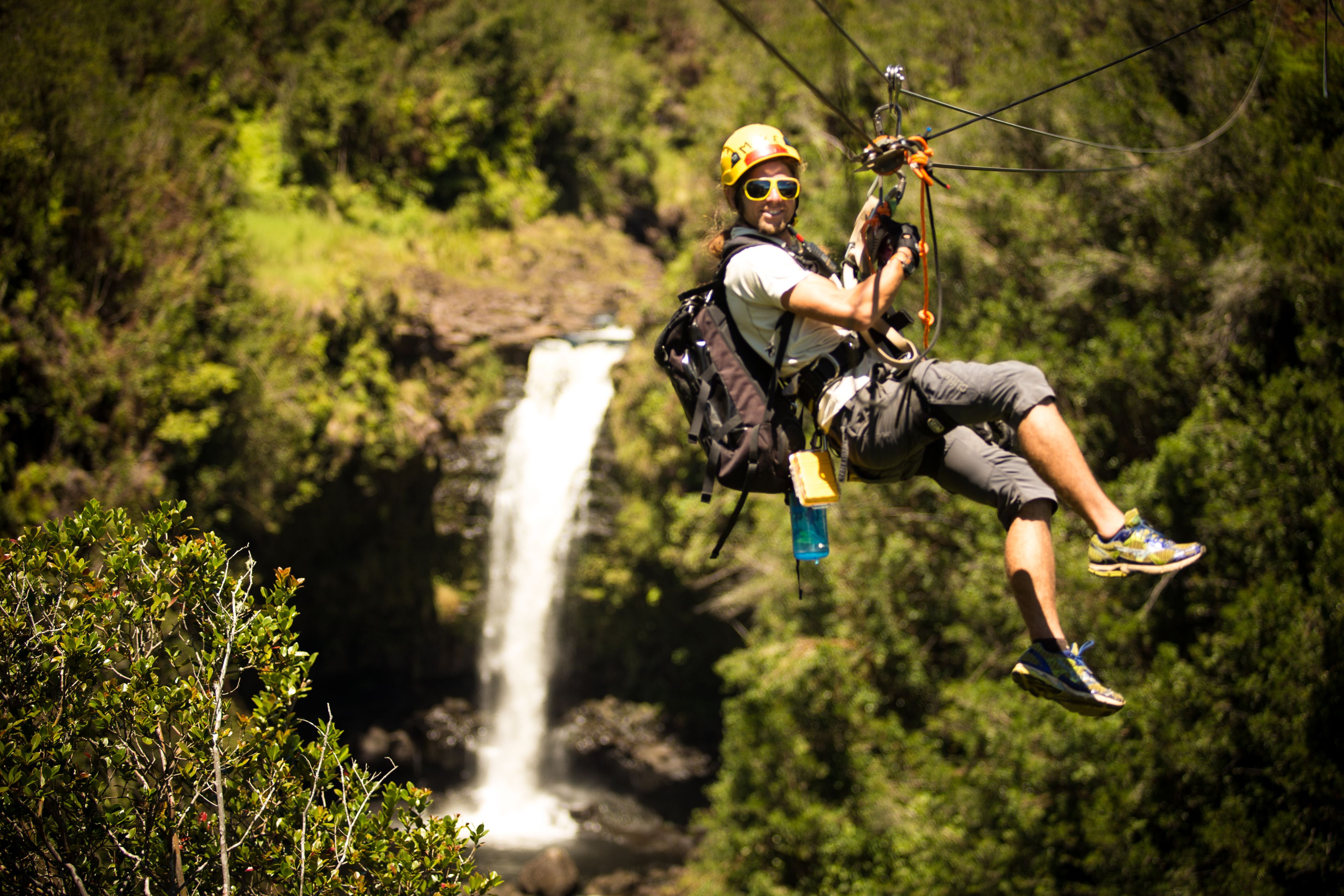 A person ziplining over a waterfall in a forest.