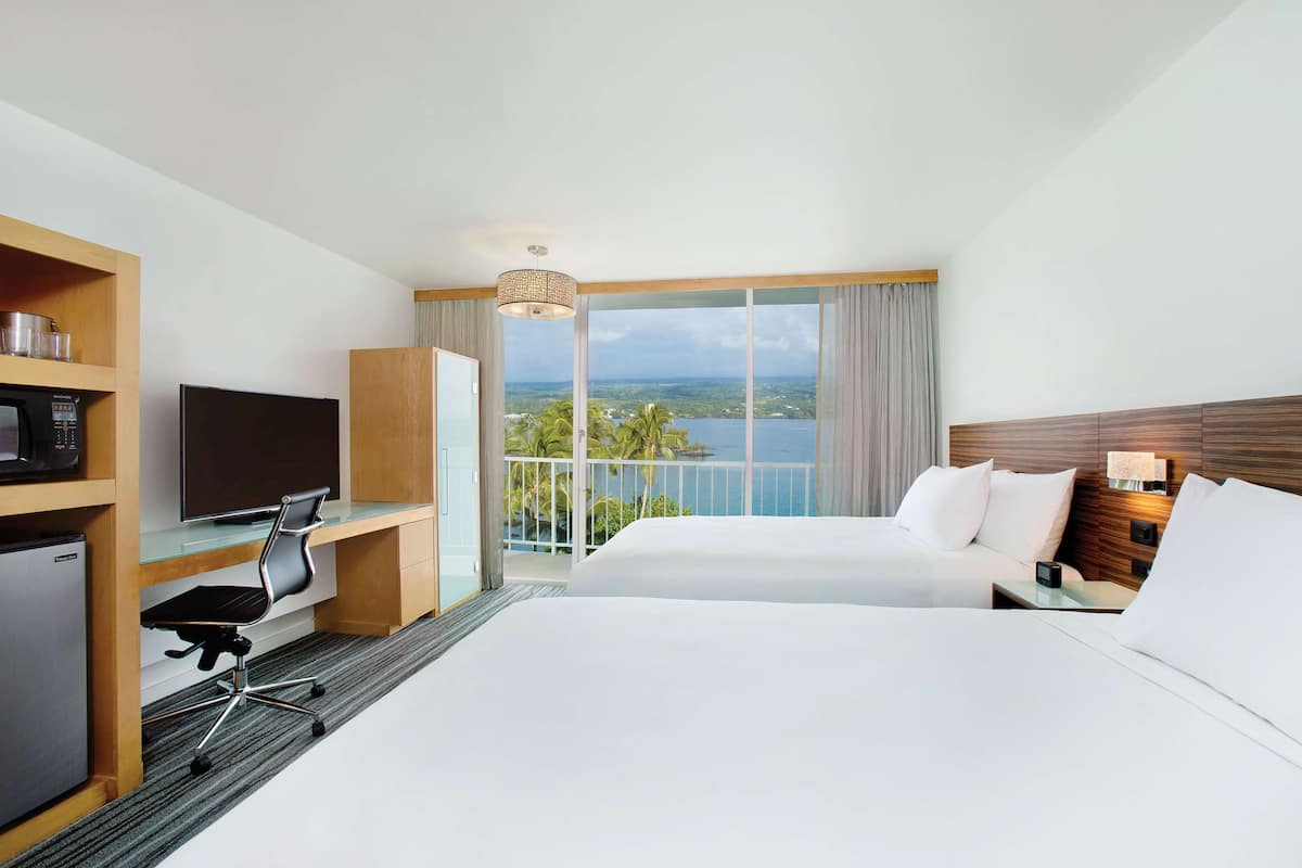 Ein Hotelzimmer mit einem Bett, einem Schreibtisch mit Computer, einem Fernseher und Blick auf den Ozean.