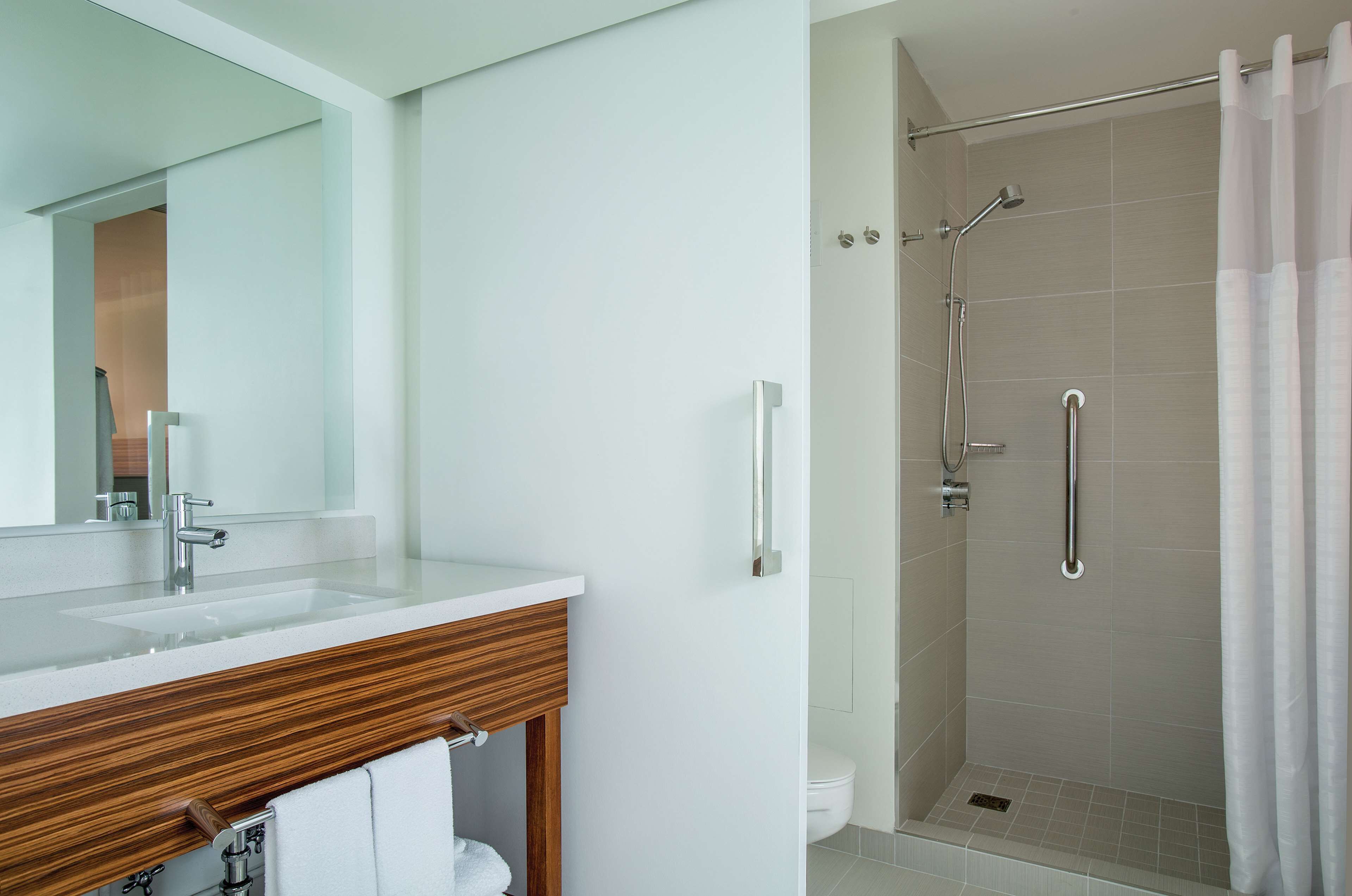 Un baño con tocador de madera, un espejo grande, ducha con puerta de vidrio y un inodoro.