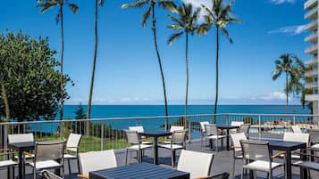 An outdoor patio with tables and chairs, overlooking a pool and the ocean.