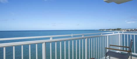A balcony with a view of the sea, a white railing, and two chairs.