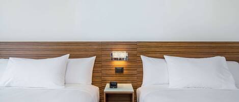A hotel room with two beds, a wooden headboard, a nightstand with a clock, and a wall-mounted light fixture.