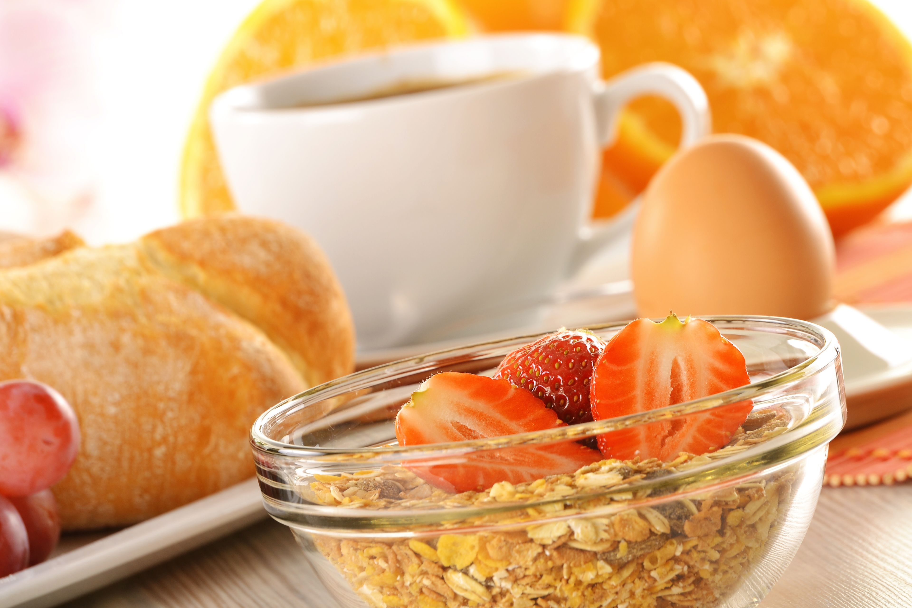 Een ontbijtje met een glazen schaal vol granola, belegd met aardbeien, een croissant, een kop koffie en een hele sinaasappel.
