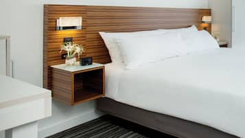 A hotel room with a wooden headboard, a bedside table with a lamp, a clock, and a framed picture on the wall.