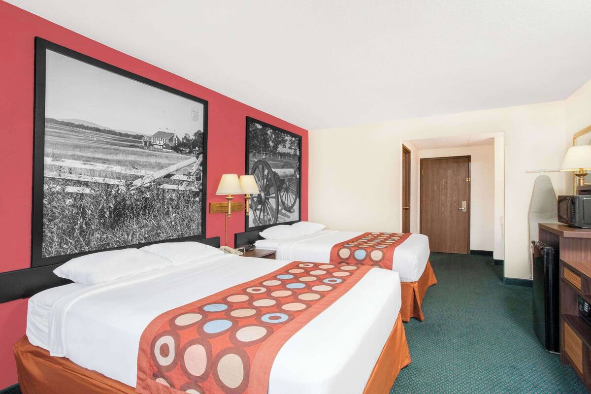 A hotel room with two beds, a desk with a computer, a TV, and two wall-mounted lamps.