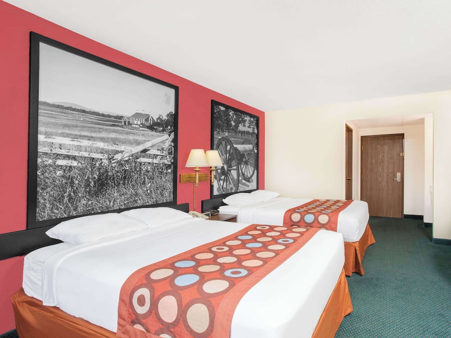 A hotel room with two beds, a desk with a computer, a TV, and two wall-mounted lamps.