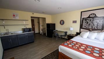 A hotel room with a bed, a desk, a chair, a refrigerator, a microwave, and a sink.