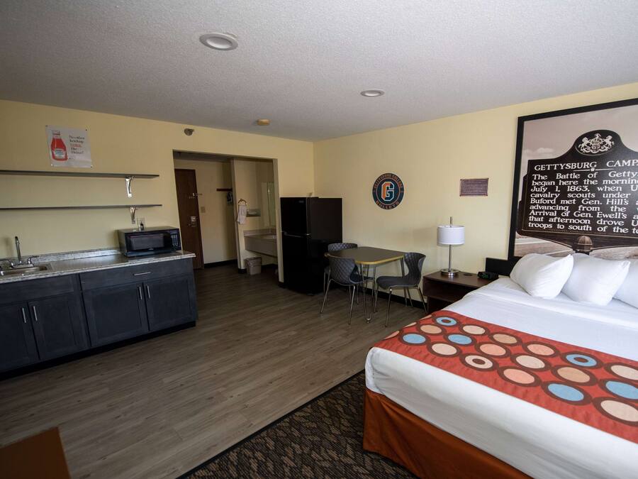 A hotel room with a bed, a desk, a chair, a refrigerator, a microwave, and a sink.