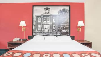 Ein Hotelzimmer mit einem Bett, zwei Nachttischen, einer Lampe auf jedem Tisch und einem großen gerahmten Bild eines Gebäudes an der Wand.
