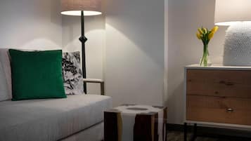 A modern living room with a grey sofa, a green pillow, a black and white abstract pillow, a wooden side table, and a lamp with a white lampshade.