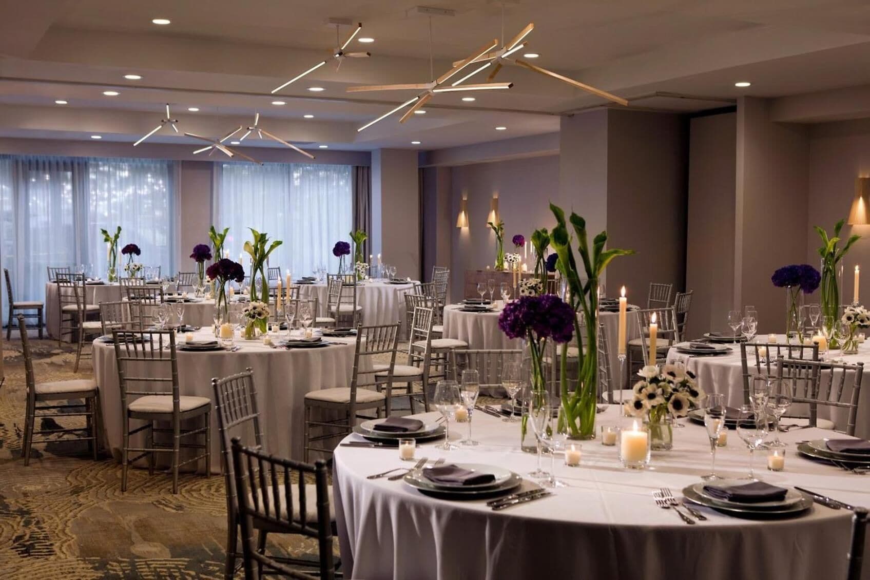 A banquet hall with round tables set for dining, featuring white tablecloths, candles, and floral centerpieces.