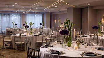 A banquet hall with round tables set for dining, featuring white tablecloths, candles, and floral centerpieces.