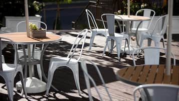 A deck with white plastic chairs and tables, some with wooden tops.