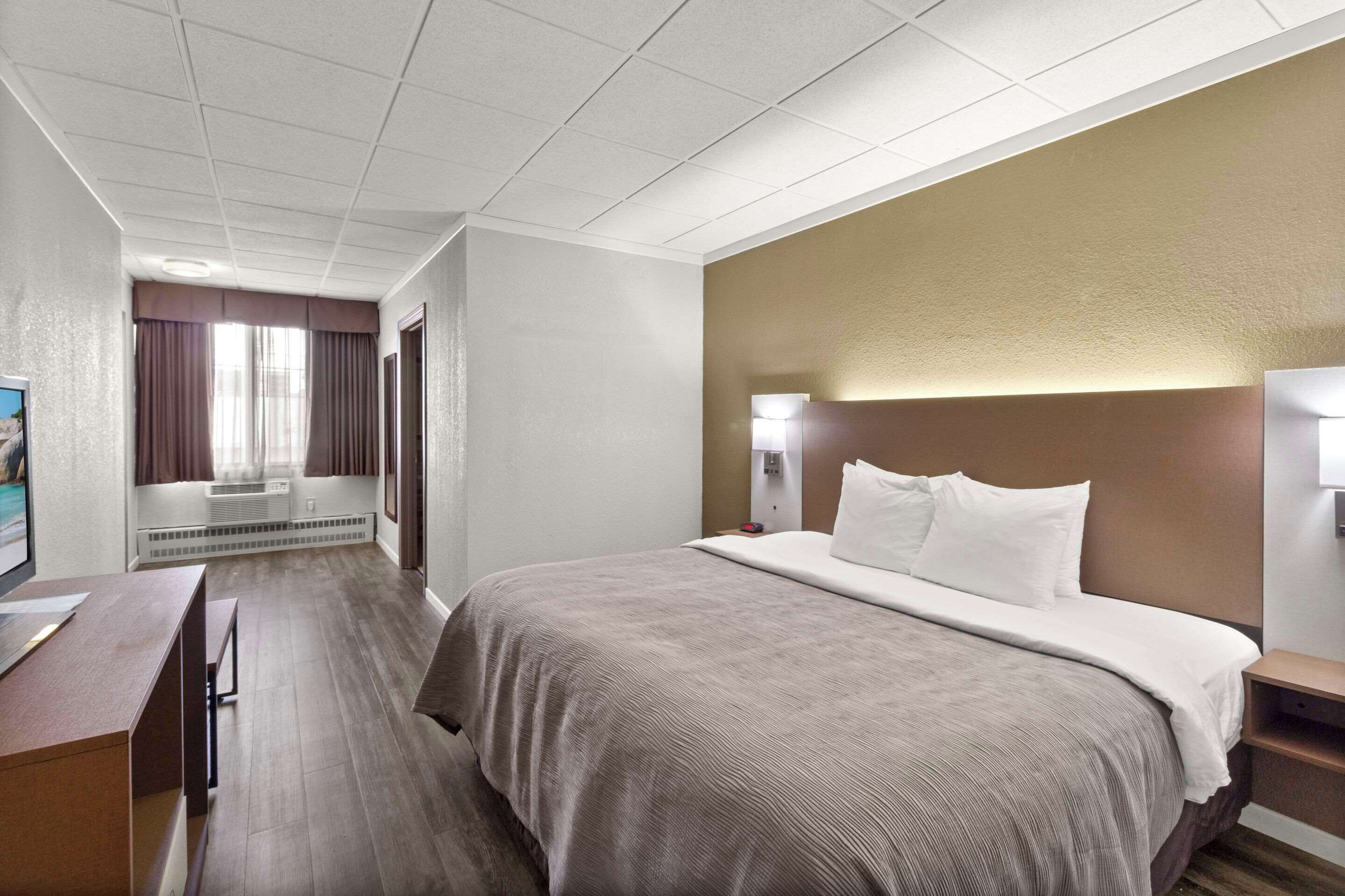 A hotel room with a bed, bedside tables, a desk, and a window with curtains.