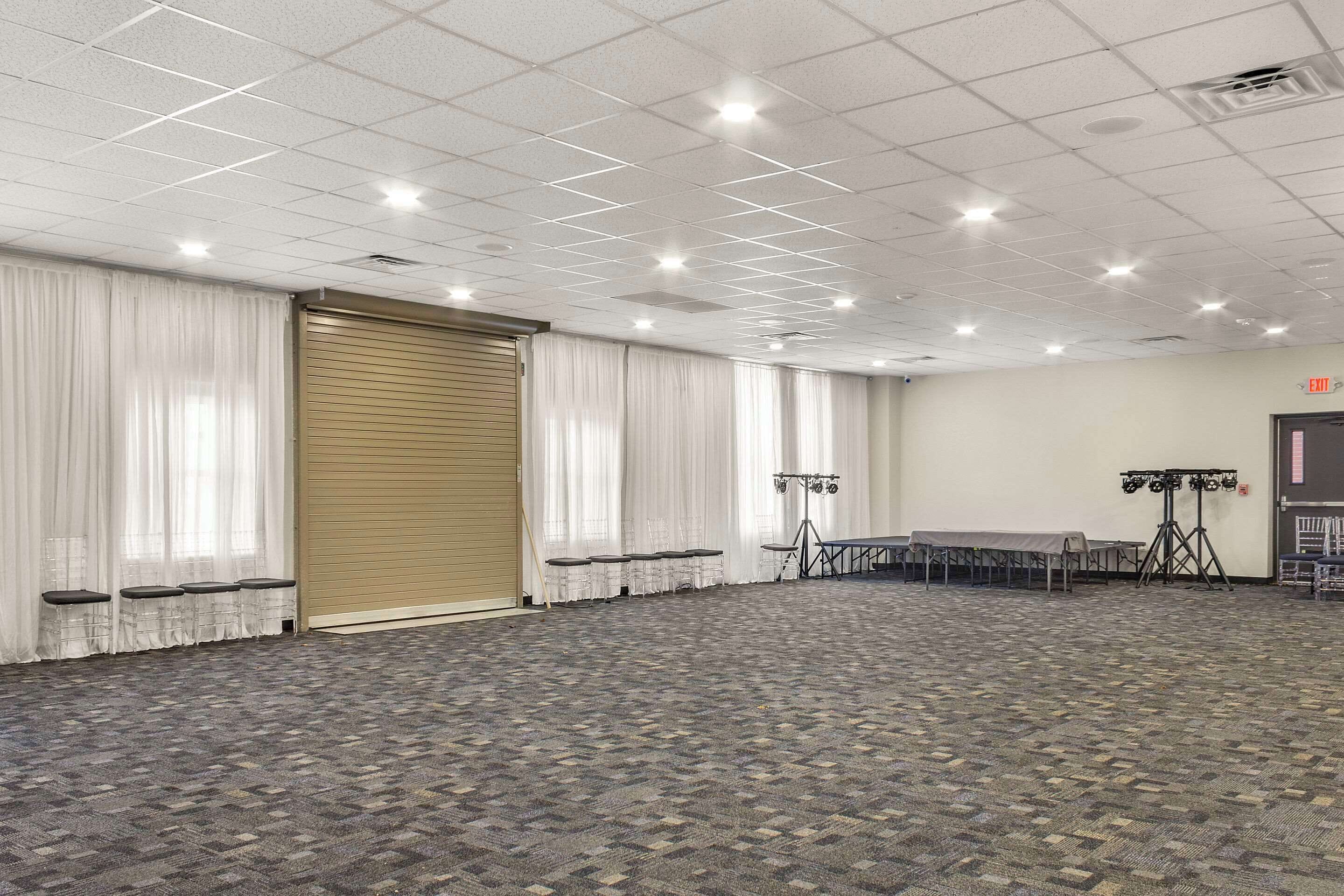 A large conference room with a patterned carpet, white curtains, and a closed sliding door.