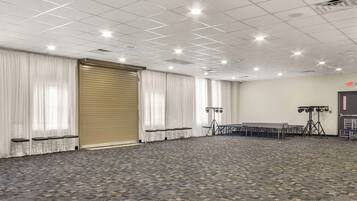 A large conference room with a patterned carpet, white curtains, and a closed sliding door.