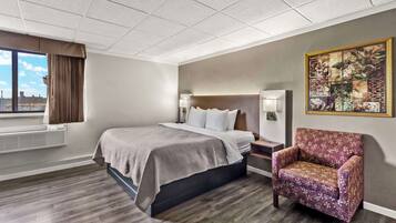 A hotel room with a bed, a chair, a nightstand, and a painting on the wall.