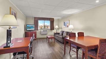 Quarto de hotel com escrivaninha de madeira, sofá, mesa de jantar e televisão.