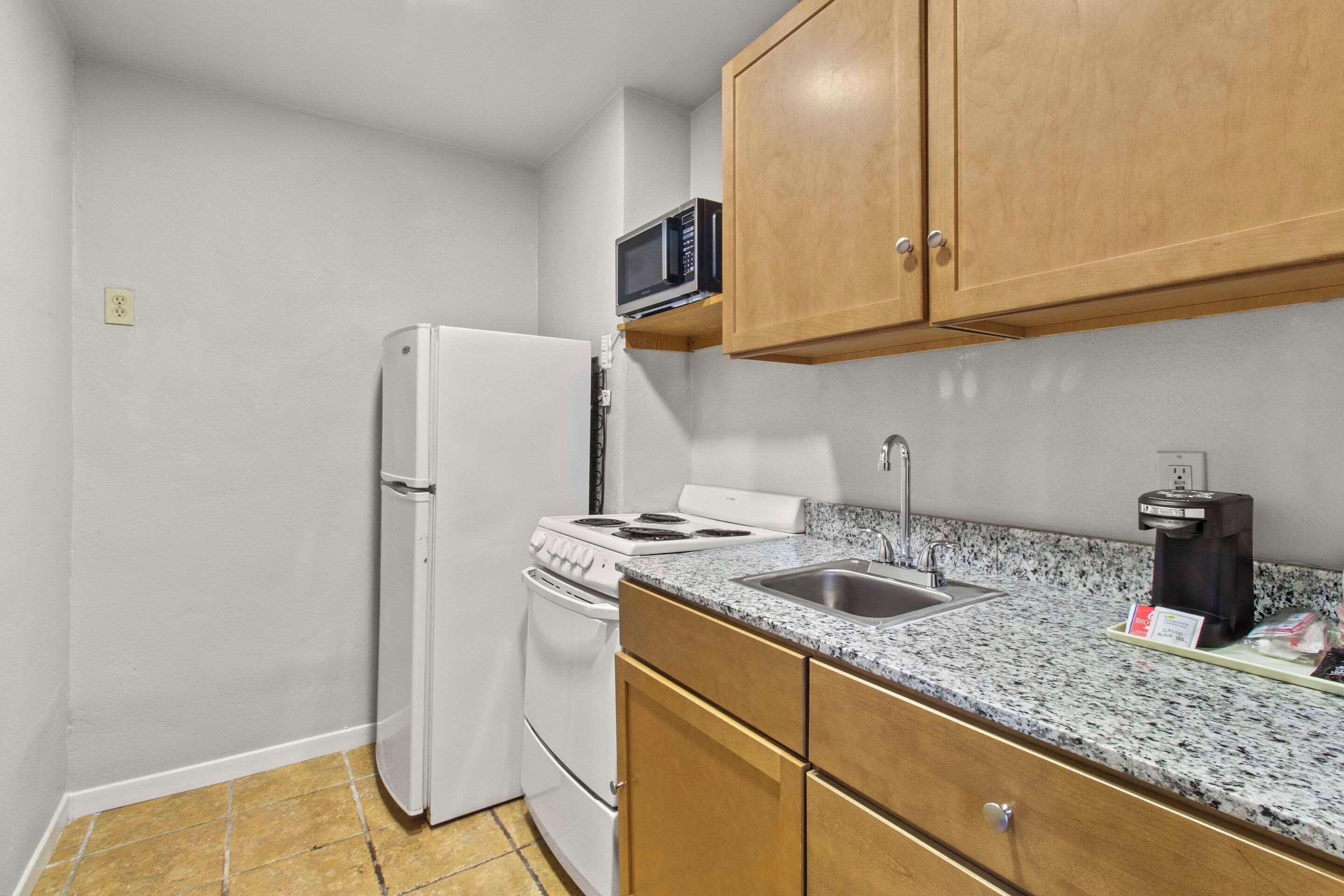 A compact kitchen with white appliances, a granite countertop, and wooden cabinets.
