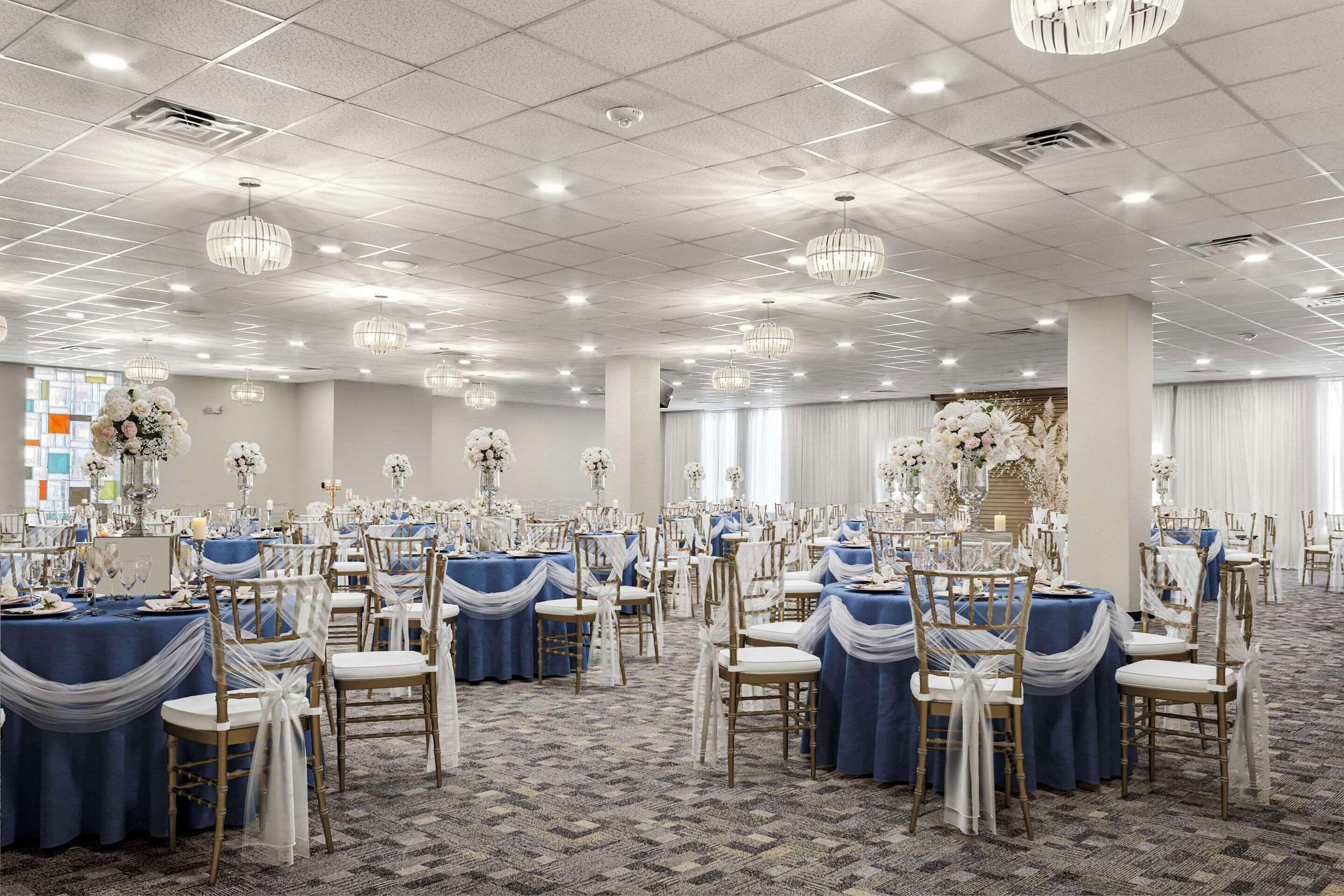 Un salón de banquetes con mesas redondas, sillas blancas y candelabros.