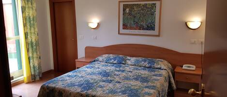 A bedroom with a floral bedspread, a wooden headboard, two bedside tables with lamps, and a framed artwork on the wall.