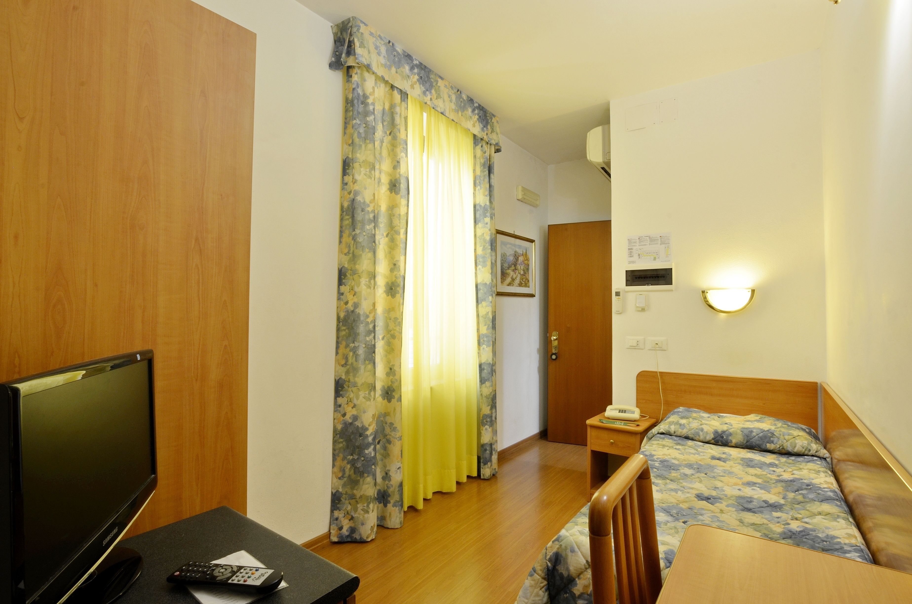 A hotel room with a bed, a TV, a desk, and a curtain.
