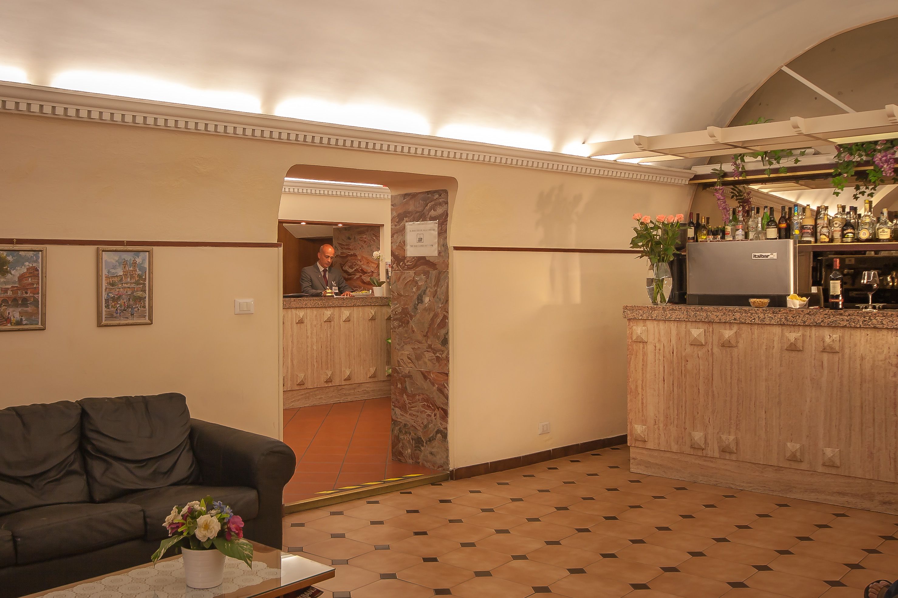 A hotel lobby with a bar area, a sofa, and a floral arrangement on a coffee table.