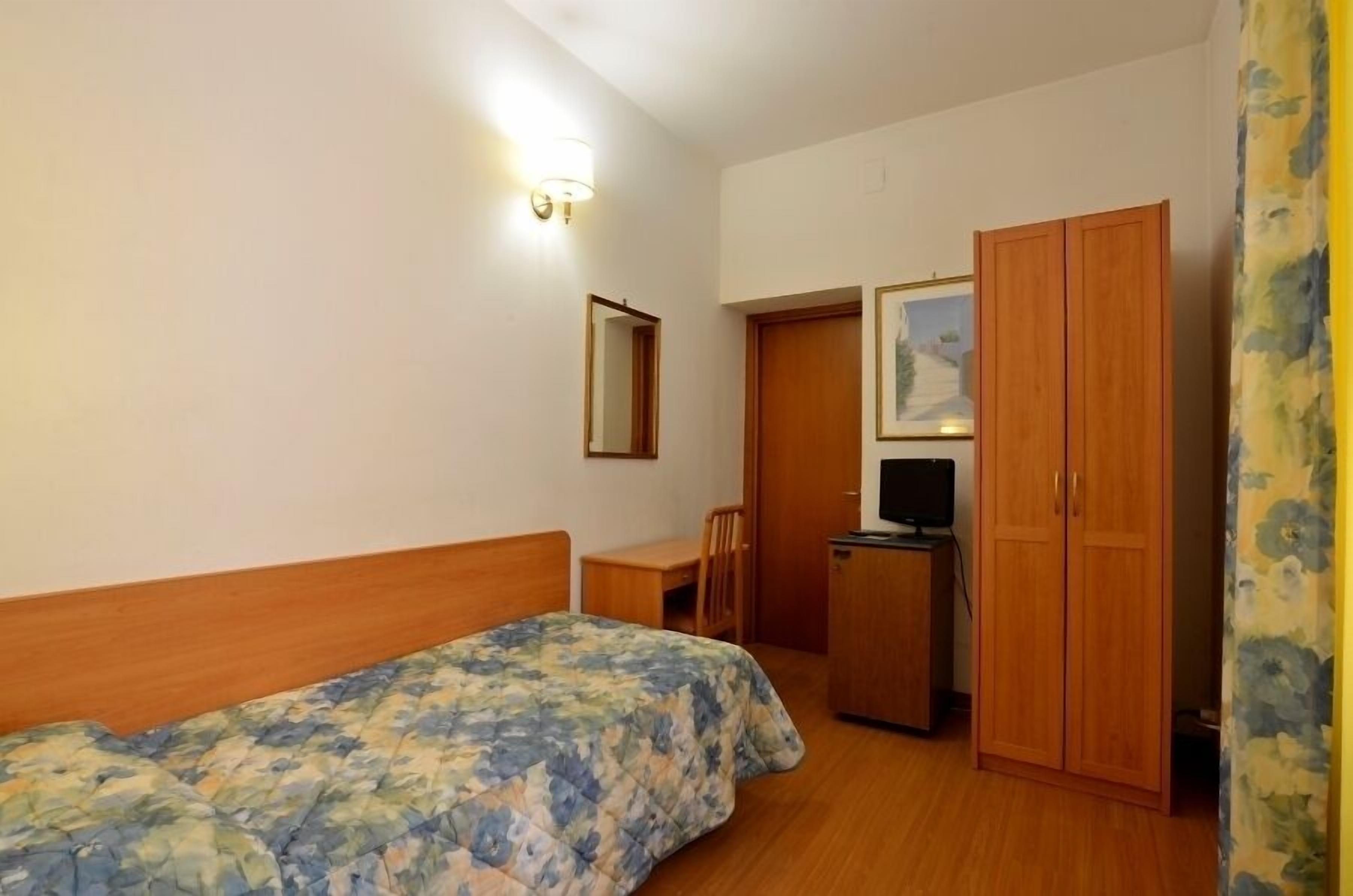 A bedroom with a bed, a desk, a television, and a wardrobe.
