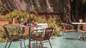 An outdoor seating area with wicker chairs and a table, surrounded by potted plants and a pool.