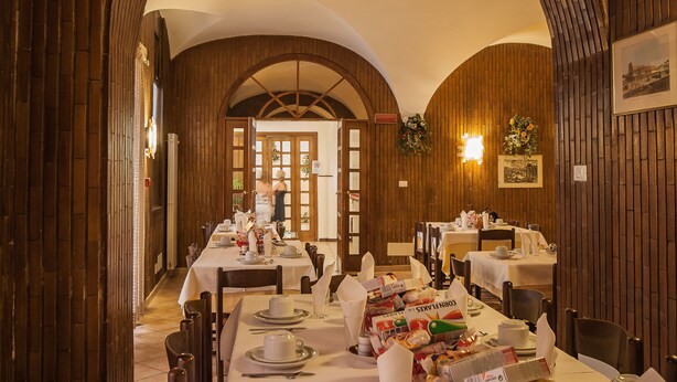 A dining area with tables set for a meal, wooden paneling on the walls, and a view of the dining room through an arched doorway.