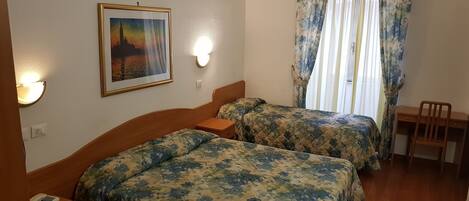 Une chambre d’hôtel avec deux lits, un bureau, une chaise, un téléphone et un tableau au mur.