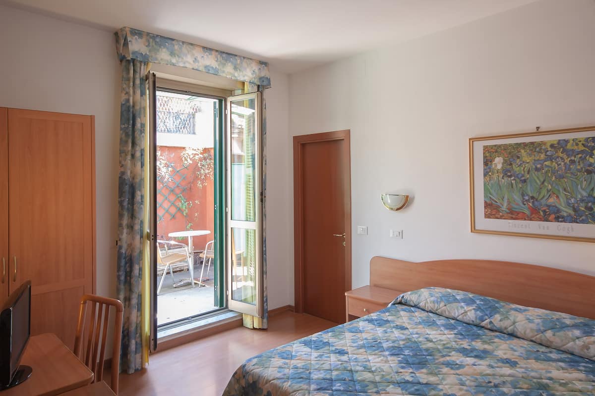 A bedroom with a bed, a desk, a chair, a door, and a window with curtains.