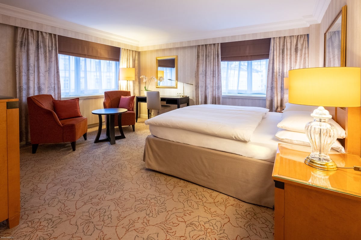 Ein Hotelzimmer mit einem großen Bett, einem Schreibtisch, einem Sessel und einem kleinen Tisch.