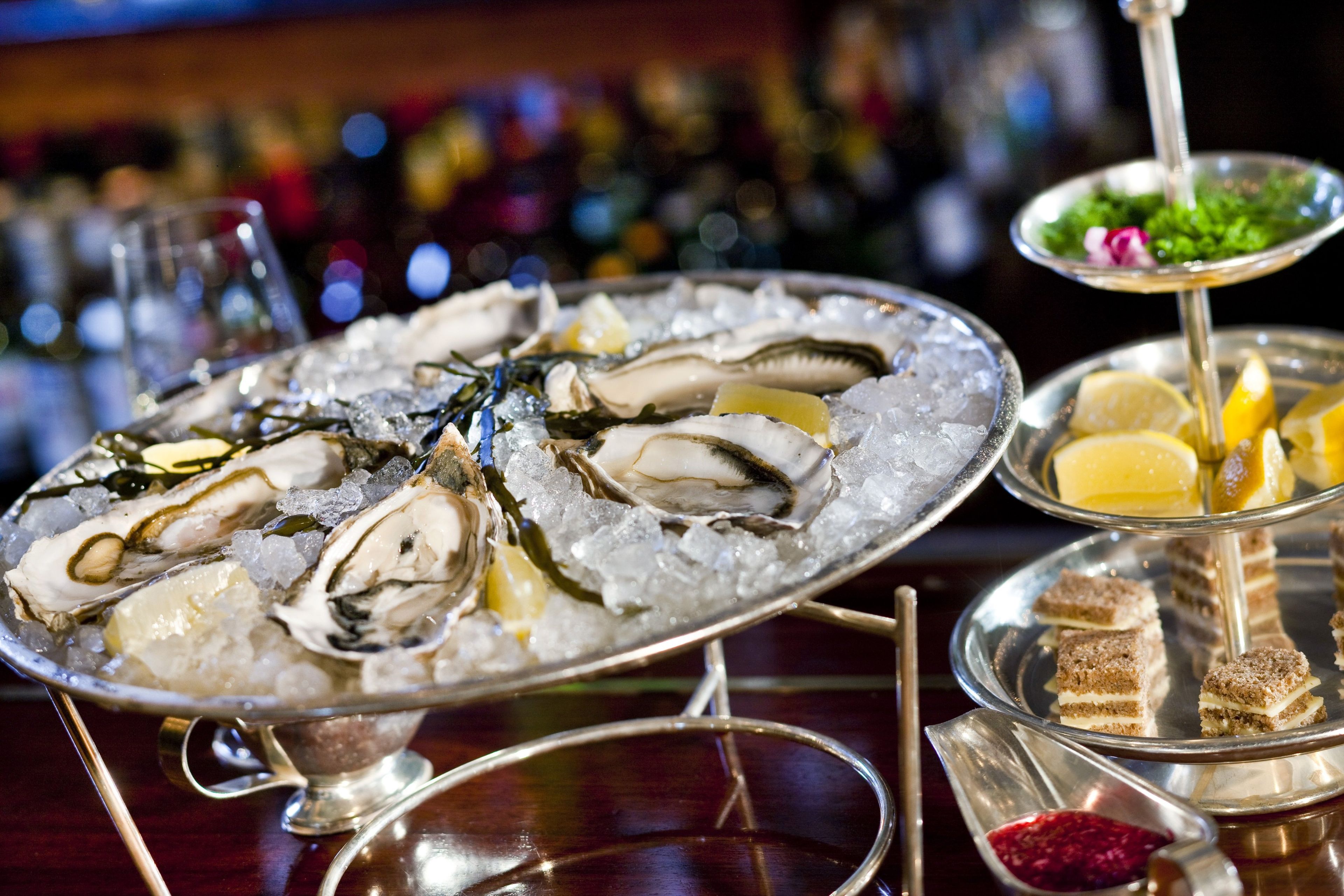 A seafood platter with oysters on ice, a small dish of lemon slices, and a dessert tray with cake and berries.