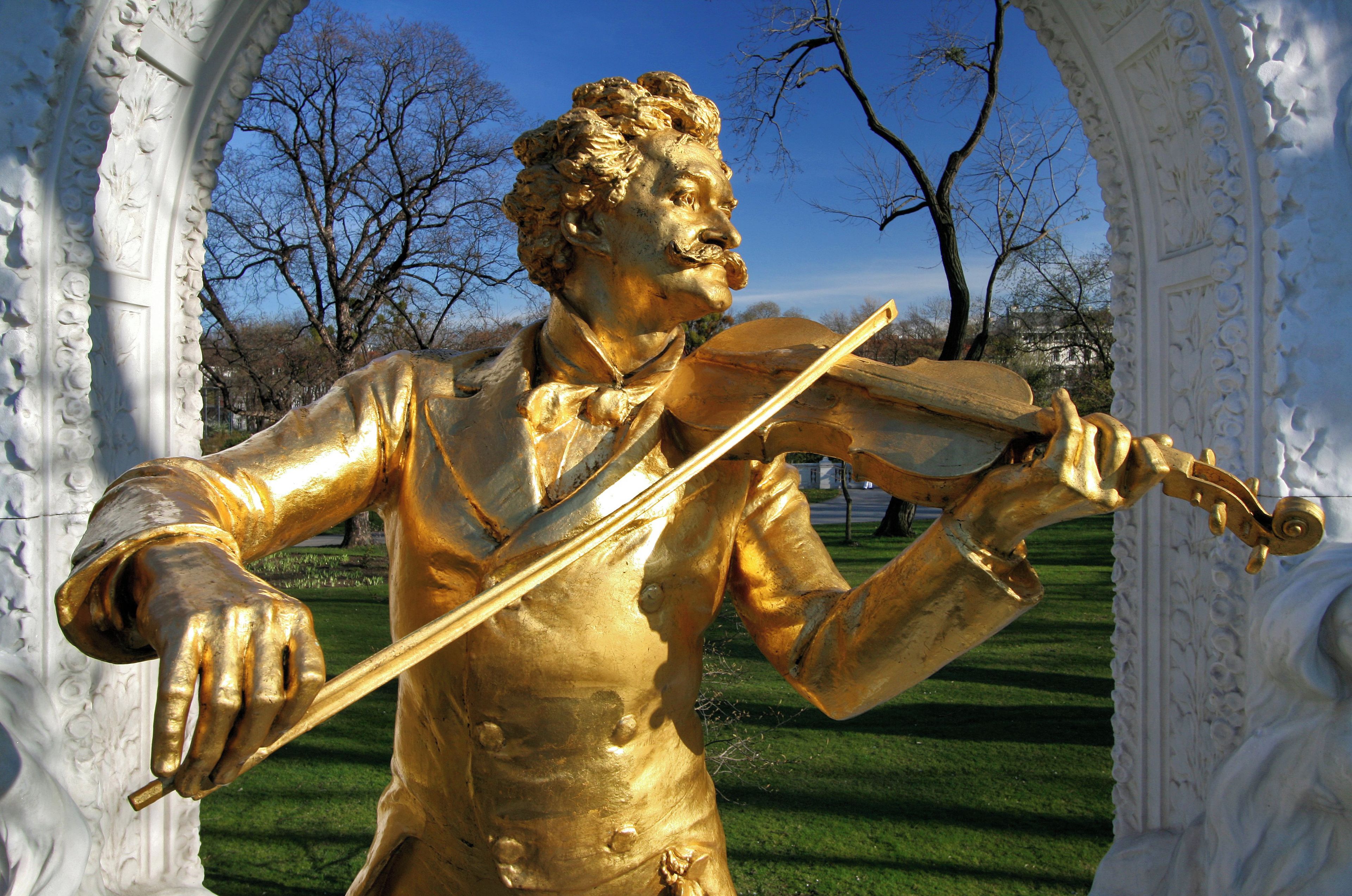 Eine goldene Statue eines Mannes, der Geige spielt, eingebettet in einen verzierten weißen Bogen.
