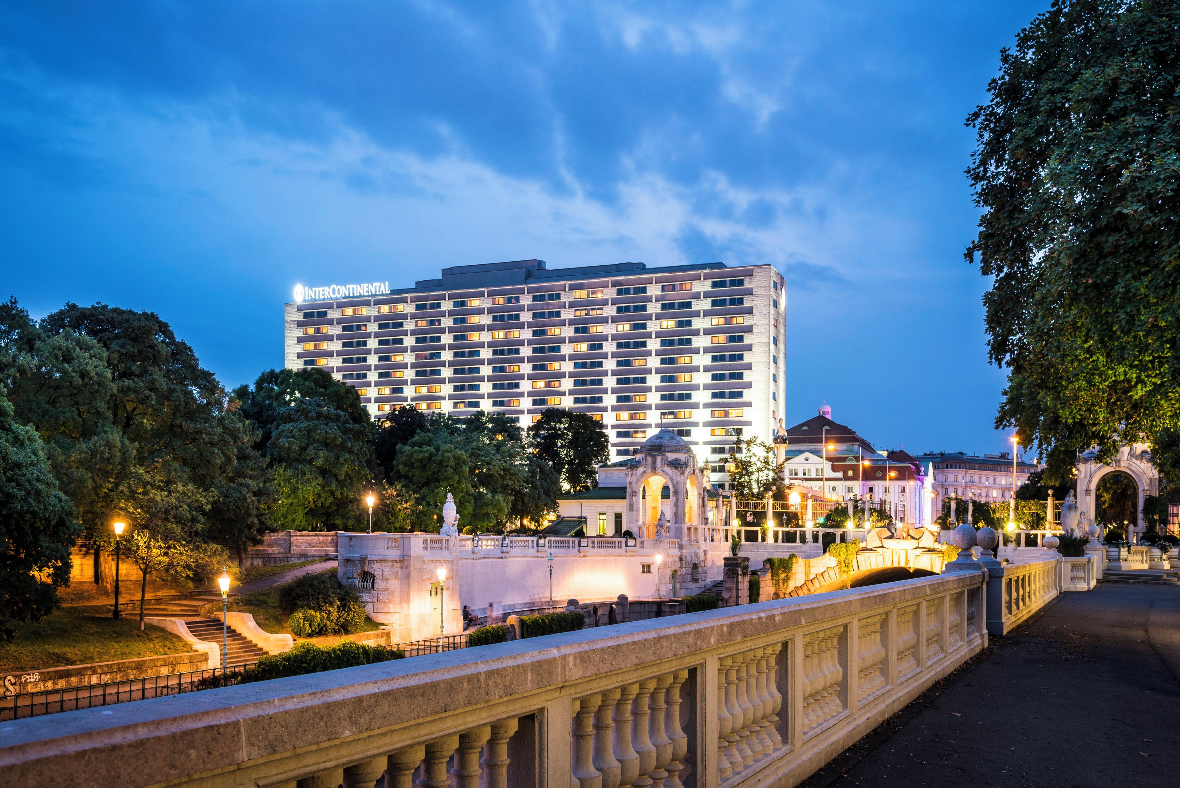Un hotel de varios pisos con una fachada moderna, un jardín bien cuidado y un puente con barandillas ornamentales.