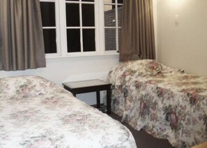 A room with two beds, a small table, and a window with curtains. - Browns Bay Olive Tree Motel & Apartment (Auckland)
