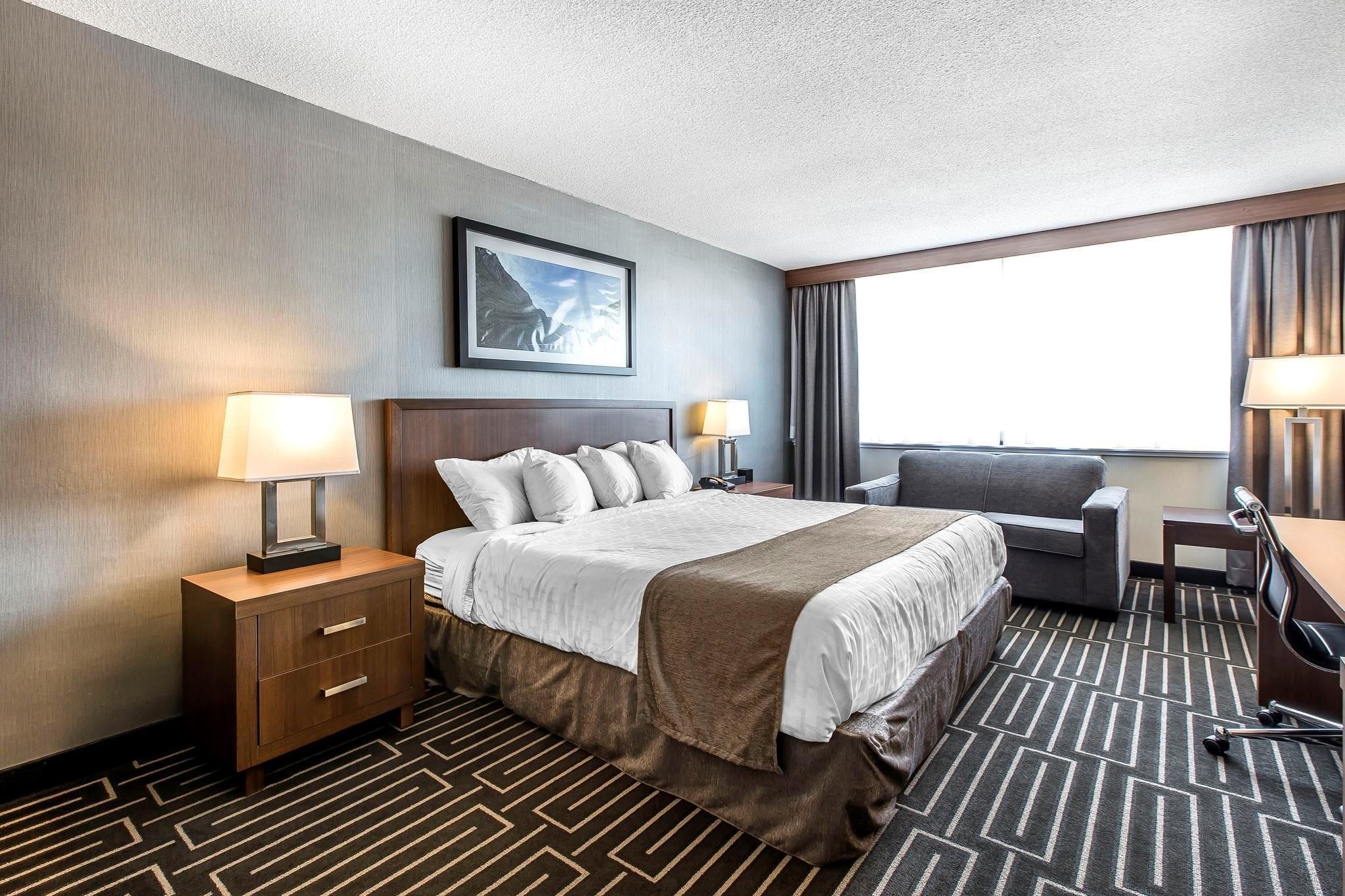 A hotel room with a large bed, a desk, a chair, and a window with curtains.